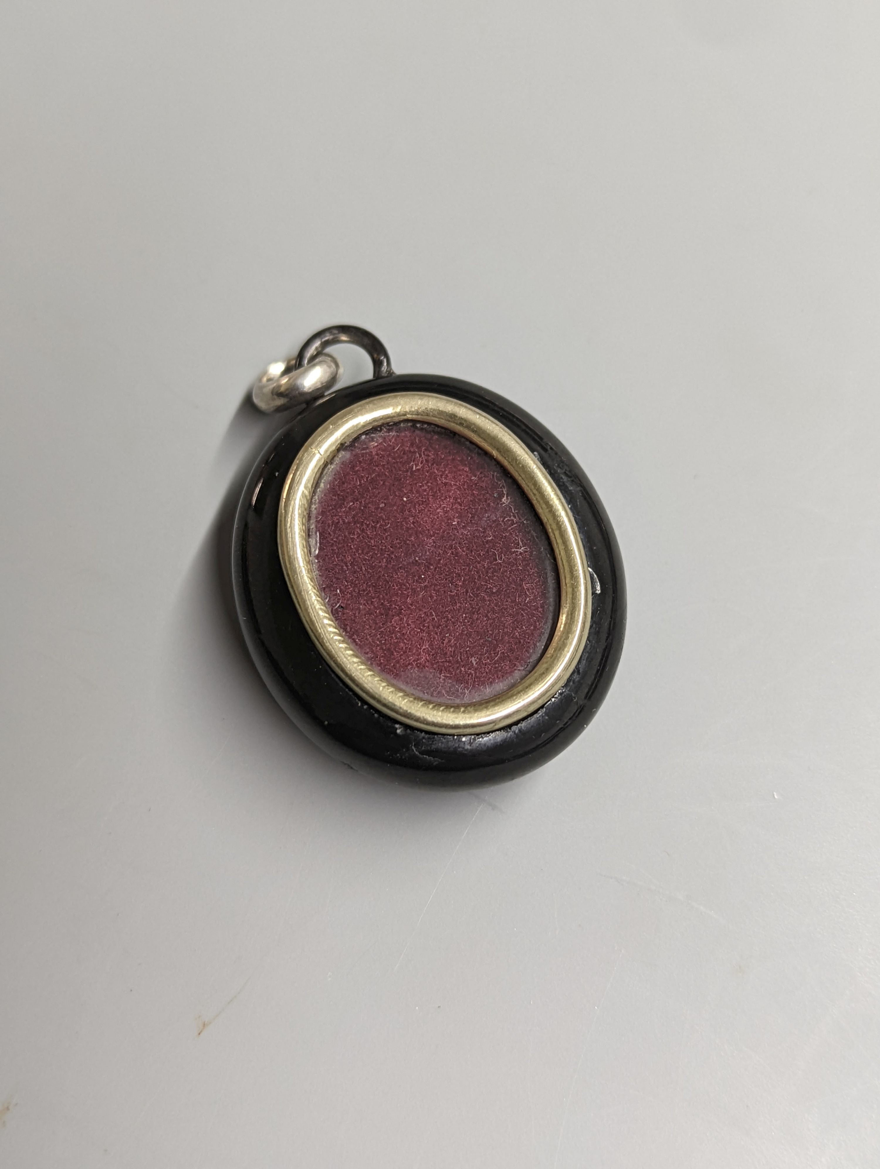 A late Victorian white metal and black enamelled oval mourning locket, with horseshoe applique and glazed back, 42mm.